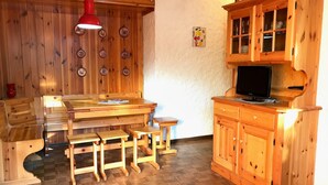 A wooden interior with a dining table, benches, a red hanging light, and a wooden cabinet with glass doors.