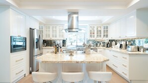 Een moderne keuken met witte kasten, een centraal eiland met krukken, roestvrijstalen apparatuur en een groot raam dat natuurlijk licht biedt.