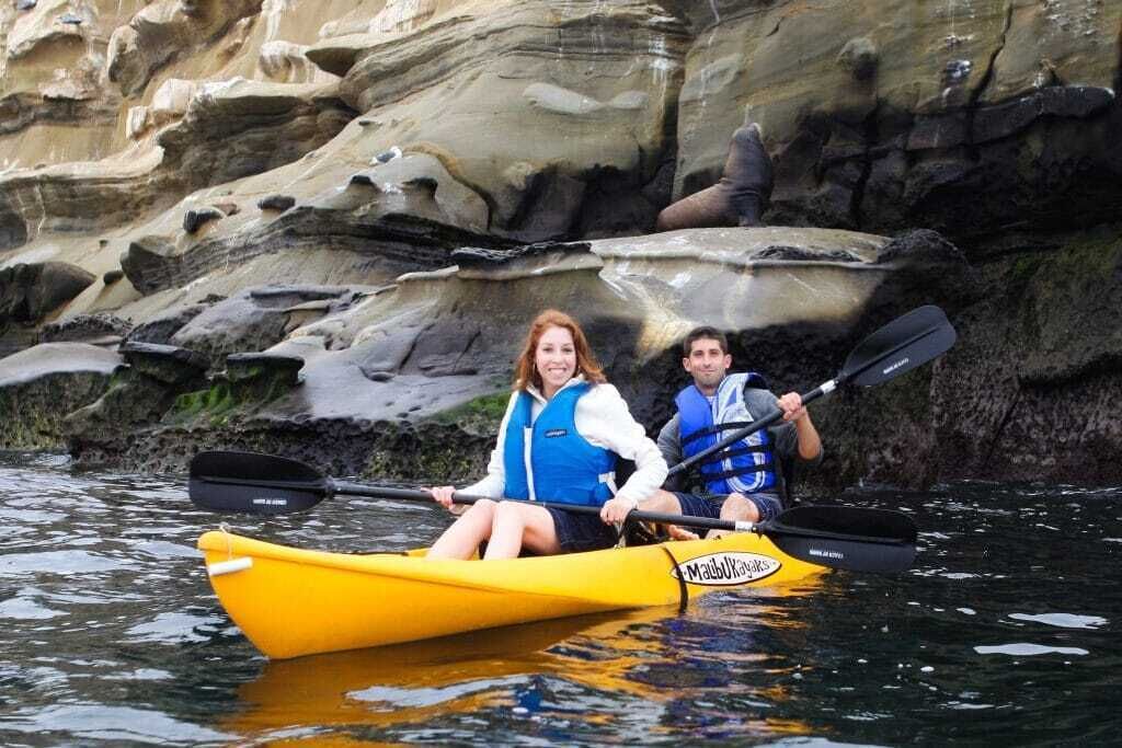 Two people kayaking in a yellow kayak with a rocky background.