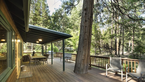 A wooden deck with outdoor furniture, a pergola, and a view of a forested area.