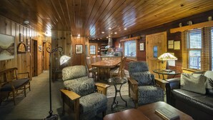 A cozy cabin interior with wooden walls, a dining area, and seating arrangements.