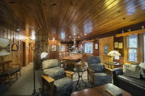 Cozy cabin interior with a warm atmosphere, featuring a seating area, dining table, and kitchen.