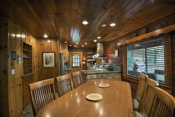 Cozy cabin-style room with a dining table, kitchen area, and large window.