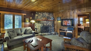 A cozy cabin interior with a stone fireplace, wooden ceiling, and a television.