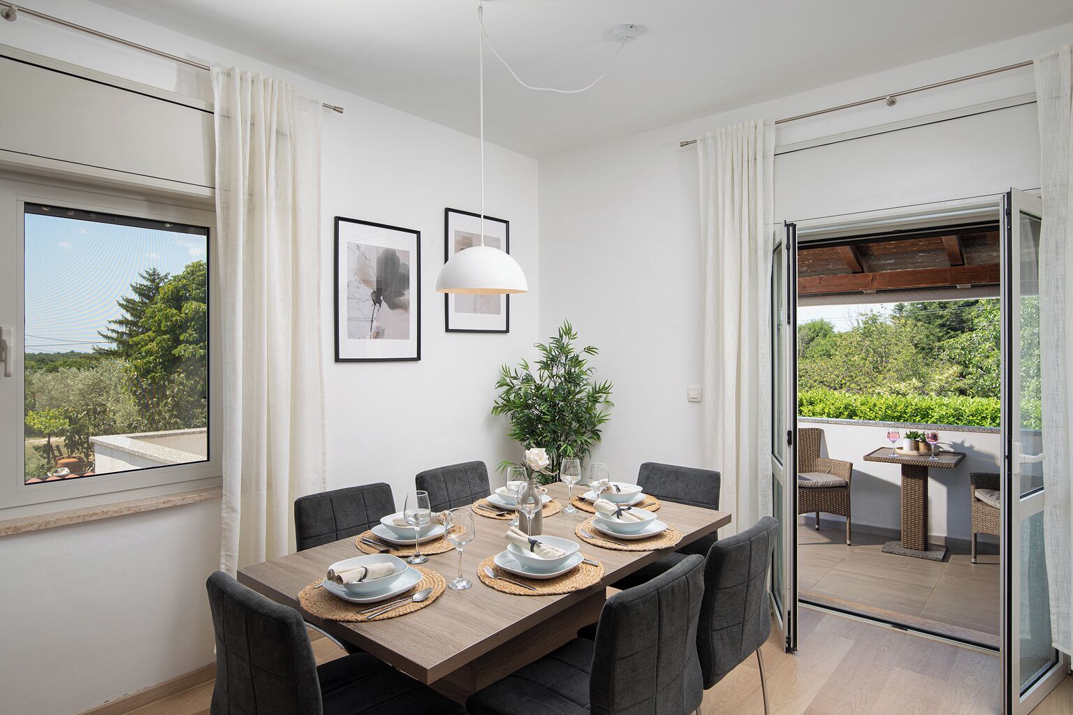 Zona pranzo con tavolo in legno apparecchiato per quattro, opere d'arte alle pareti e vista sul verde esterno.