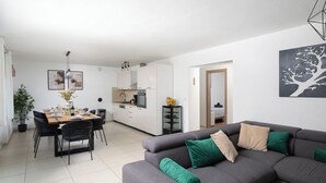 A modern living room with a gray sofa, a dining area with a wooden table, and a kitchen with white cabinets. - Beautiful holiday home with heated swimming pool, summer kitchen, WiFi, grill (Vodnjan)
