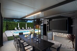 An outdoor patio with a pool, a dining table with chairs, and a flat-screen TV mounted on the wall. - Beautiful holiday home with heated swimming pool, summer kitchen, WiFi, grill (Vodnjan)