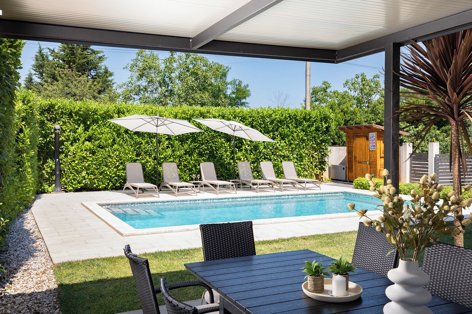 A poolside area with a pool, lounge chairs, umbrellas, and a table with potted plants.