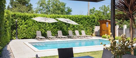 A poolside area with a pool, lounge chairs, umbrellas, and a table with potted plants.