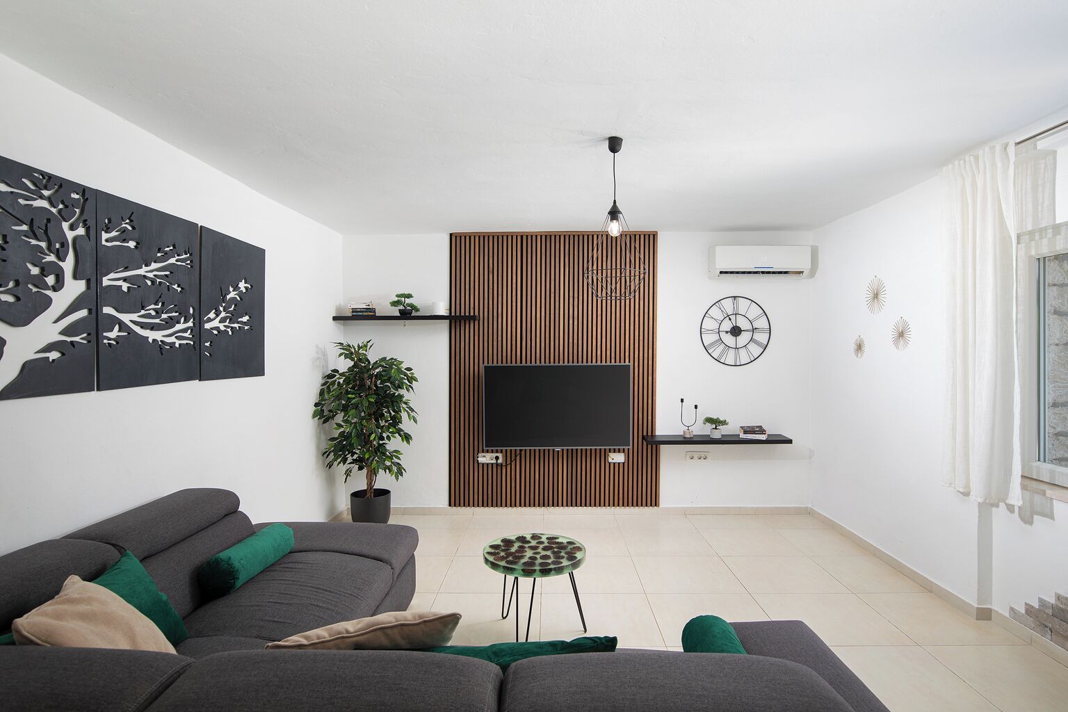 A modern living room with a grey sofa, a potted plant, a flat-screen TV, and a wooden panel wall.