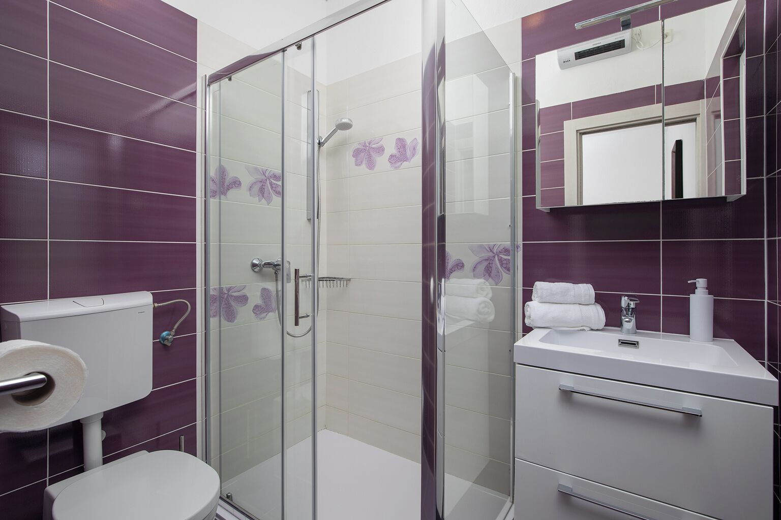 Une salle de bain moderne avec une douche à parois de verre, des toilettes, un lavabo avec un miroir et des serviettes.