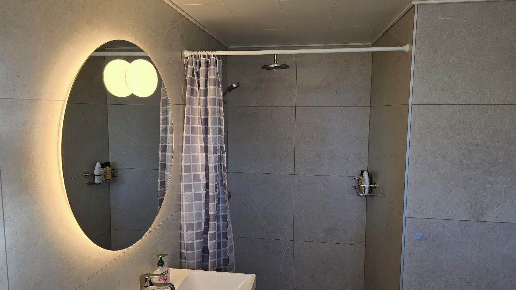A bathroom with a large mirror, a shower, and a sink.