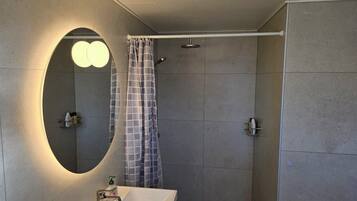 A bathroom with a large mirror, a shower, and a sink.