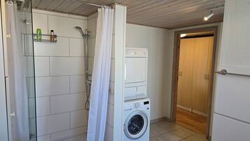Un baño pequeño con ducha, lavadora y puerta de madera.