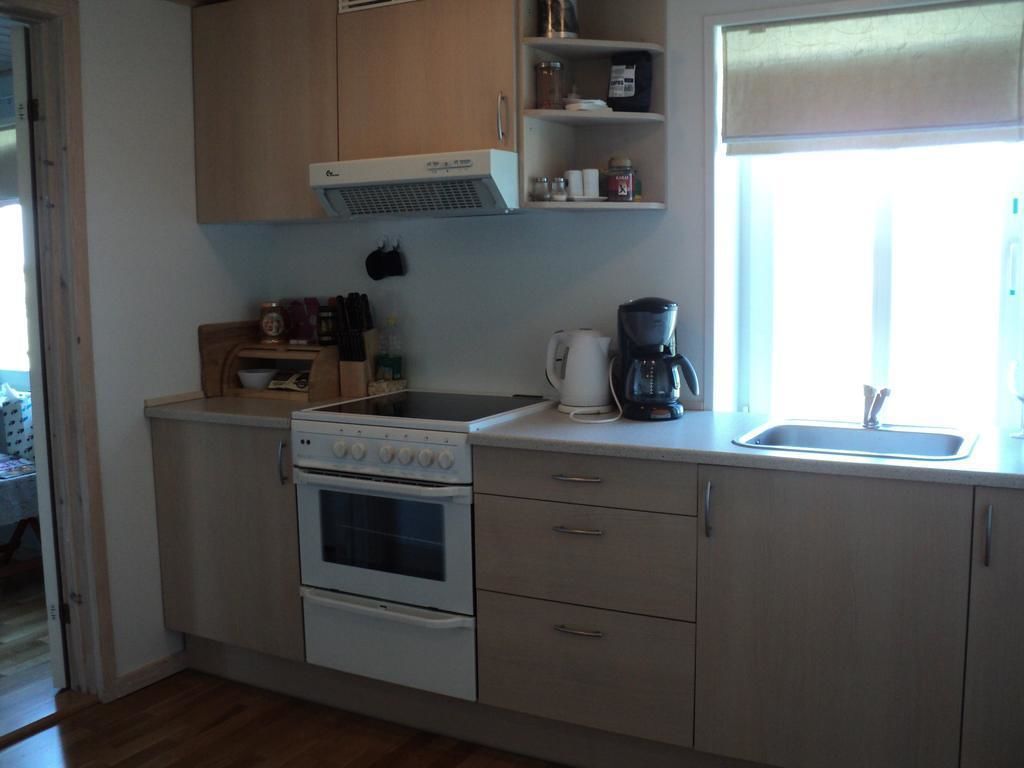 Een kleine keuken met een fornuis, oven en koffiezetapparaat. Er zijn kastjes en een raam dat voor natuurlijk licht zorgt.