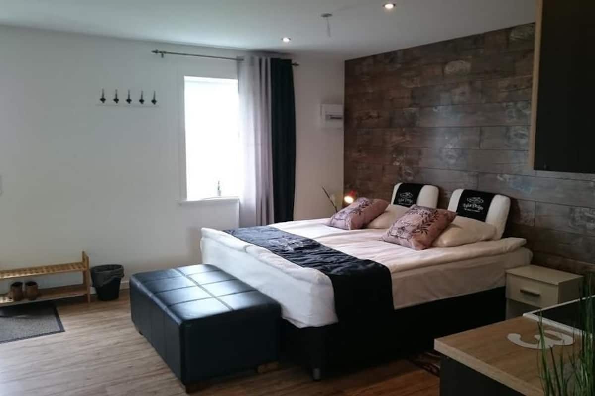 Um quarto moderno com uma cama grande, um banco, uma mesa pequena e uma parede de madeira.