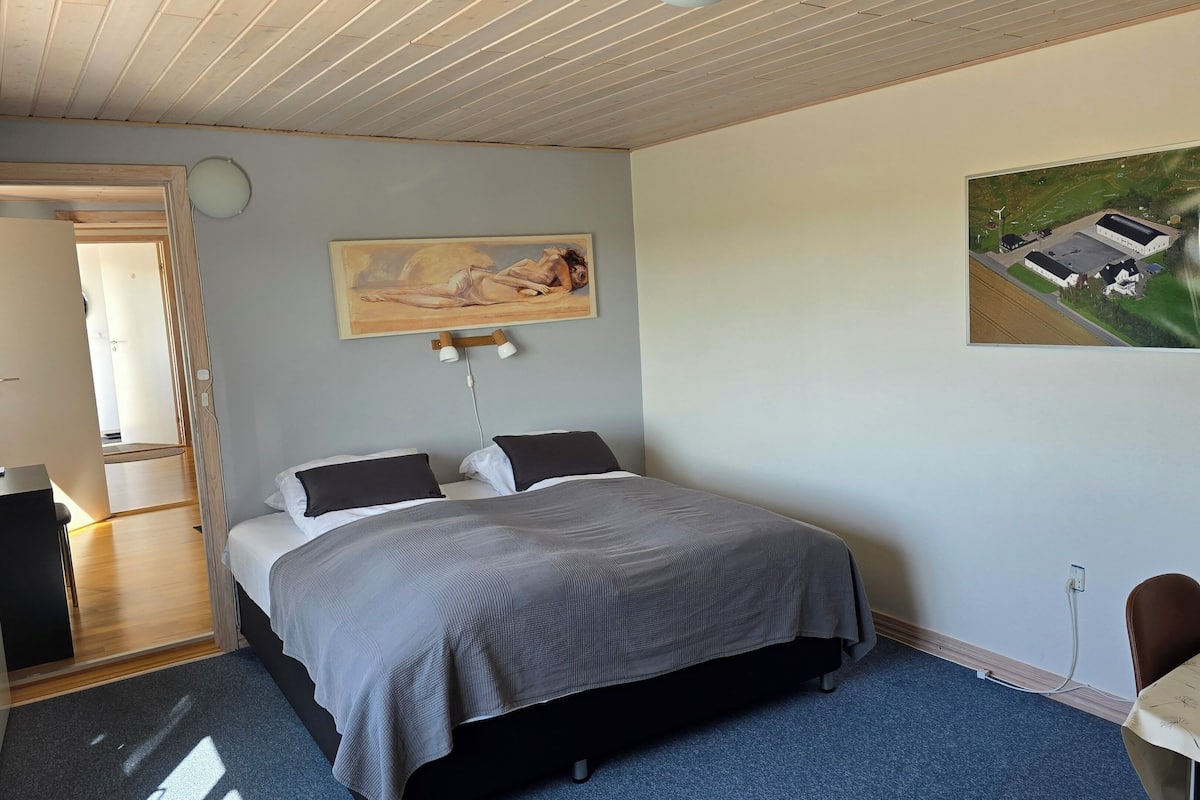 Um quarto com cama, um quadro, escrivaninha e uma cadeira.