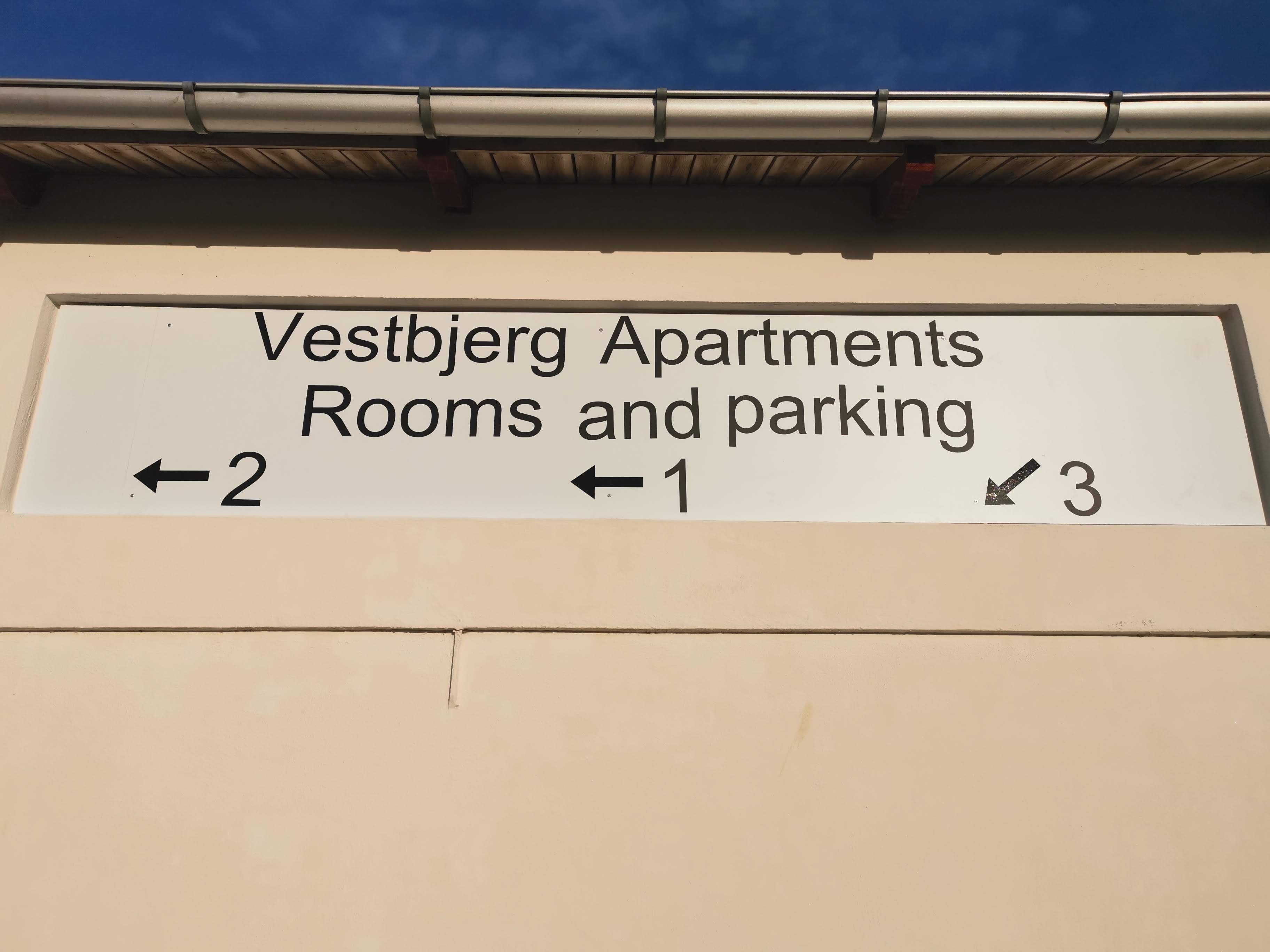 A sign for Vestbjerg Apartments indicating directions to rooms and parking.