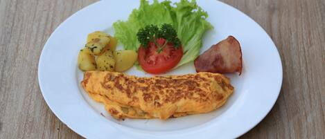 Une assiette contenant une omelette, des pommes de terre, de la laitue, une tomate et une tranche de jambon, le tout posé sur une table en bois.