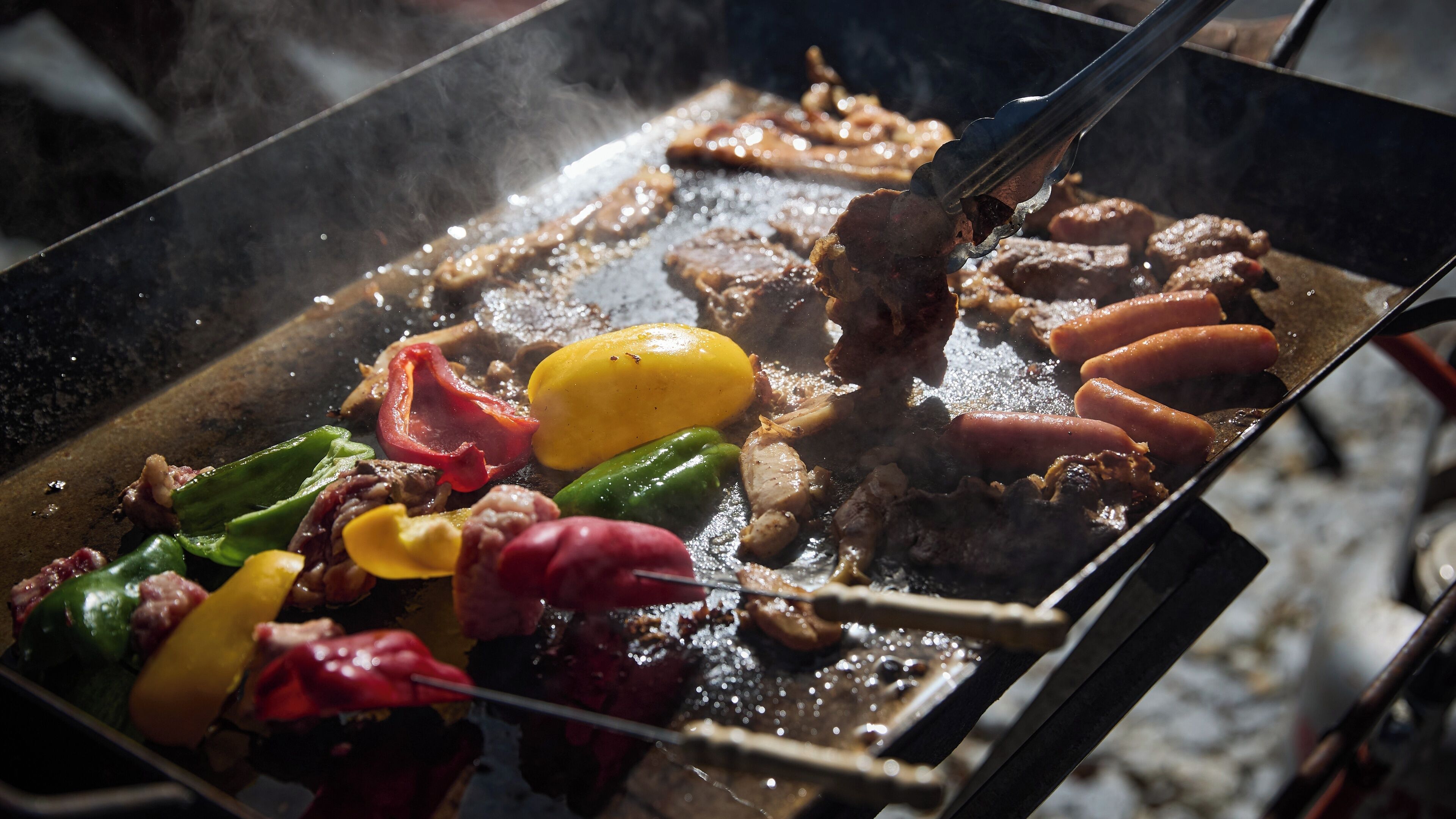 Una parrilla con diversos tipos de carne y verduras asándose.