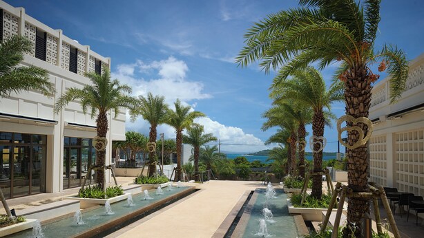 A resort courtyard with palm trees, a water feature, and a view of the sea. - RERESO Okinawa churaumi (Motobu)