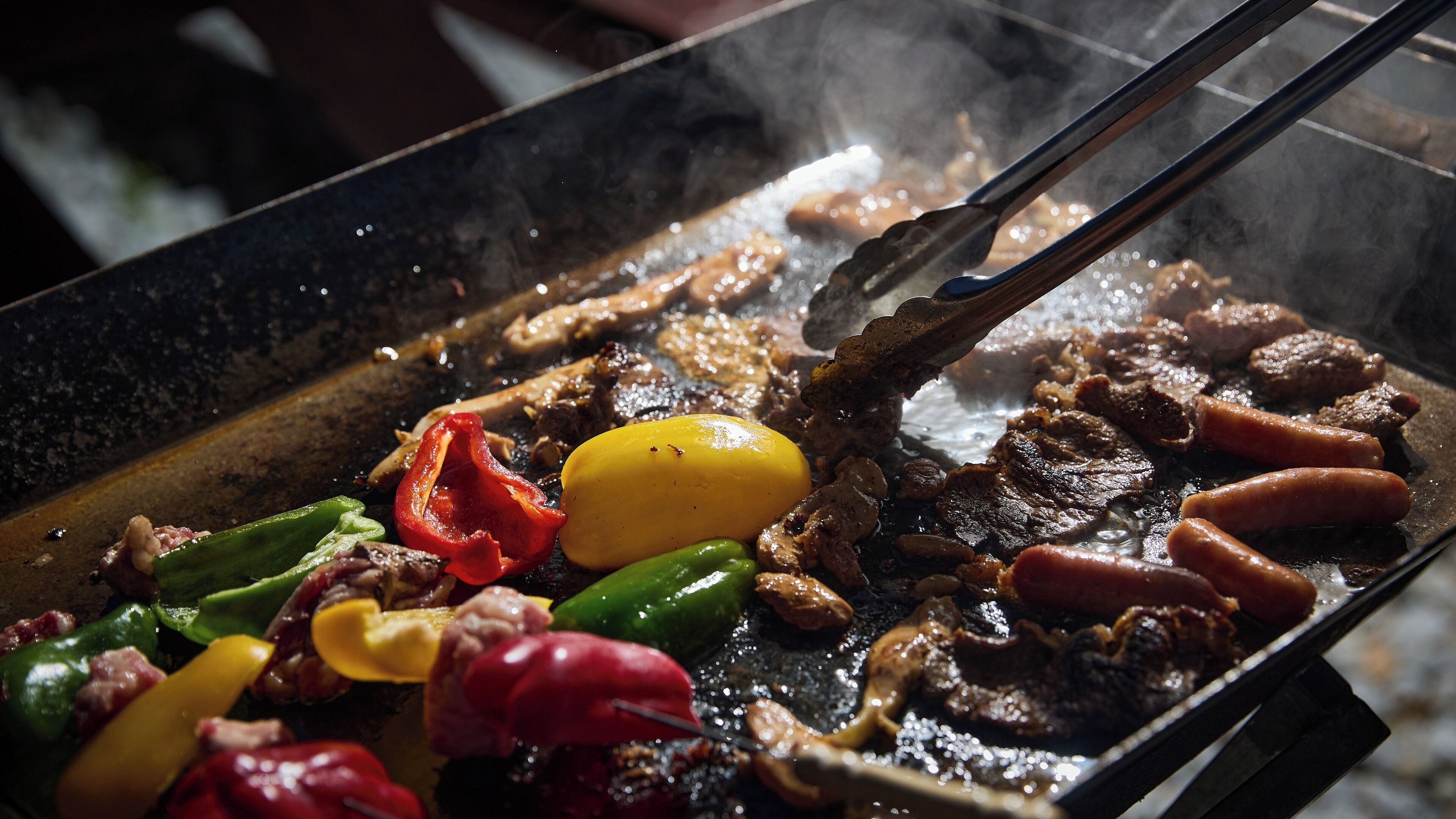 A close-up of a grill with various meats and vegetables sizzling.