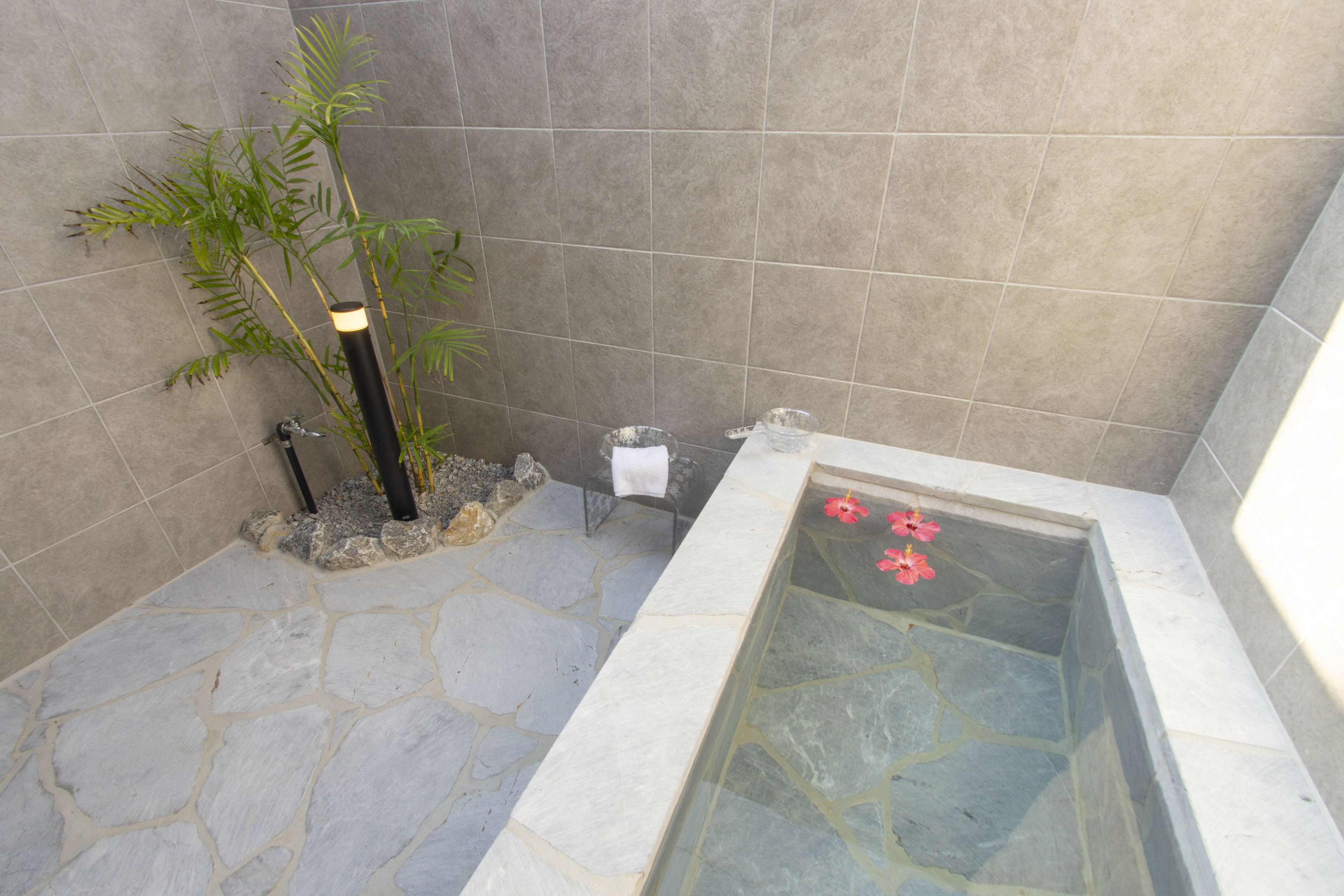 Un baño con suelo de piedra, bañera de hidromasaje con mampara de vidrio, una planta de bambú y un perchero.