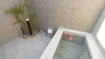 Un baño con suelo de piedra, bañera de hidromasaje con mampara de vidrio, una planta de bambú y un perchero.