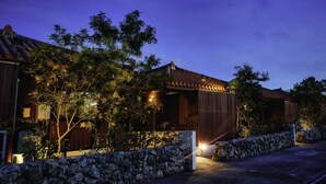 A traditional wooden house with a tiled roof, surrounded by stone walls and trees. - RERESO Okinawa churaumi (Motobu)