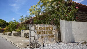 A sign for "CANOPUS MOTOBU" with a stone wall and a building in the background. - RERESO Okinawa churaumi (Motobu)