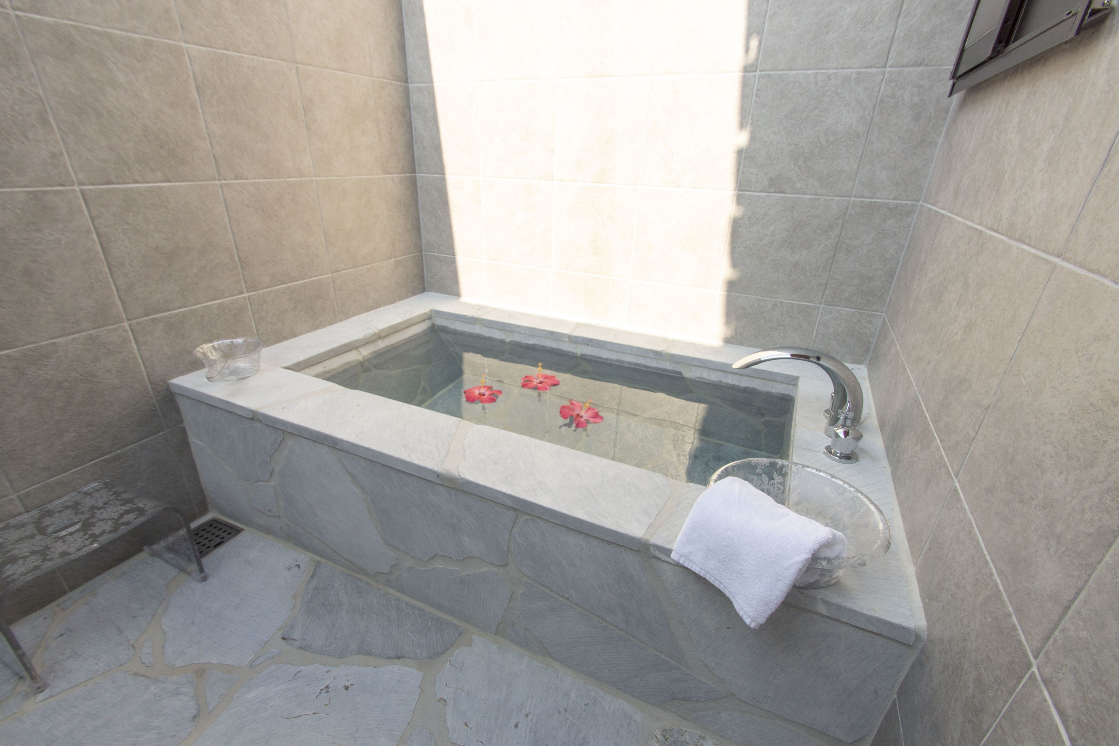A stone bathtub with a glass enclosure, a white towel, and red flowers.