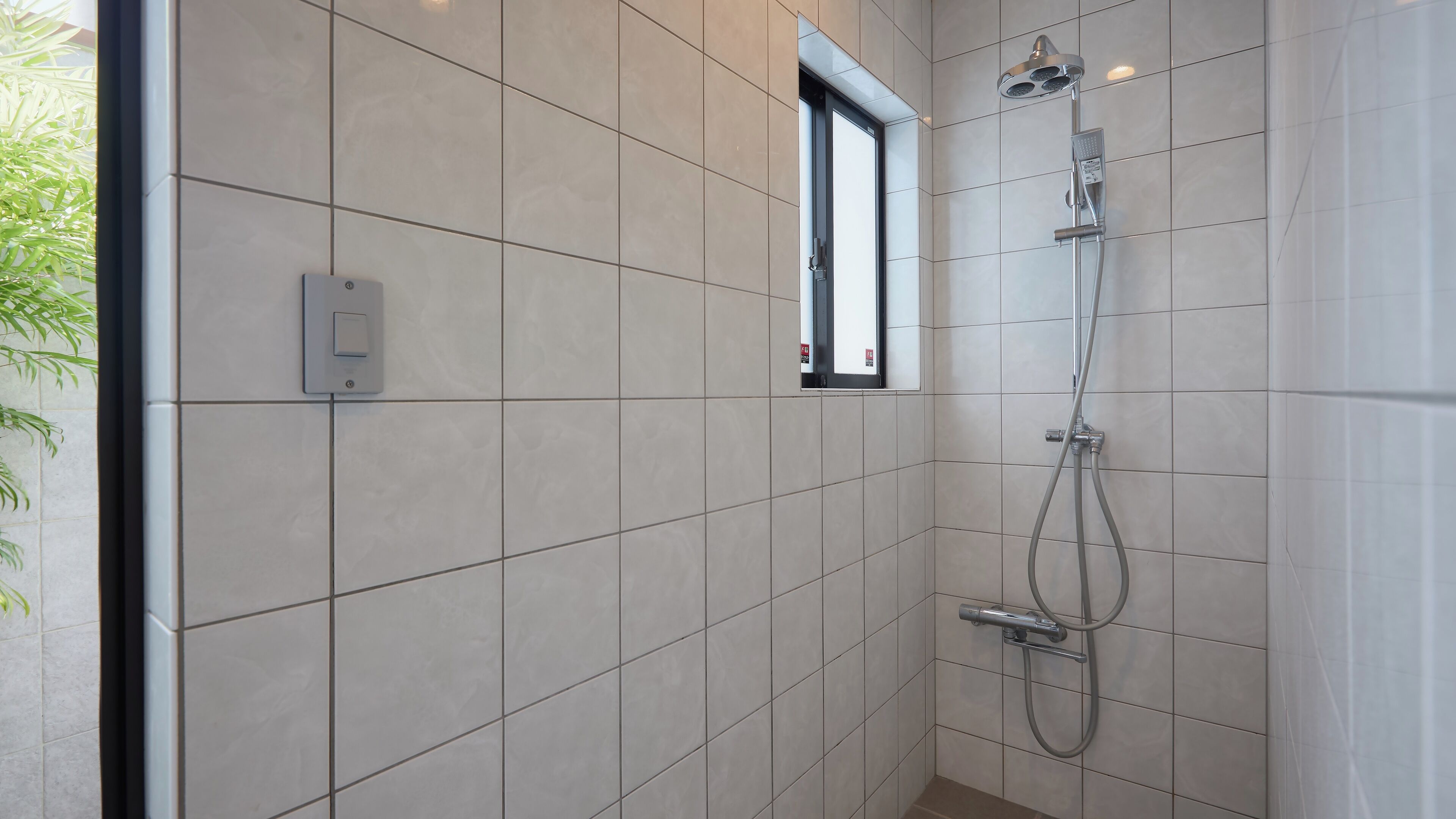A modern bathroom with a shower, tiled walls, and a window.