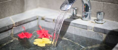 Un baño con una bañera, un grifo y dos flores en el agua.