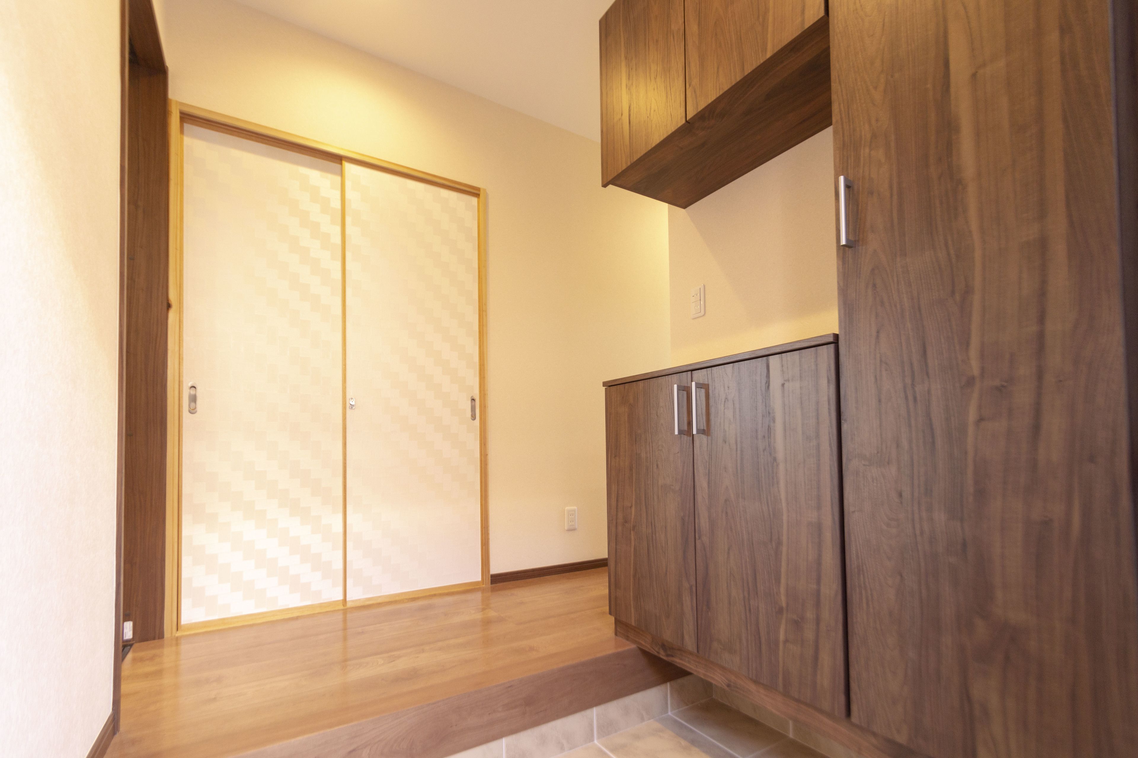 A hallway with wooden flooring, a sliding door with a geometric pattern, and a wooden cabinet with two doors.