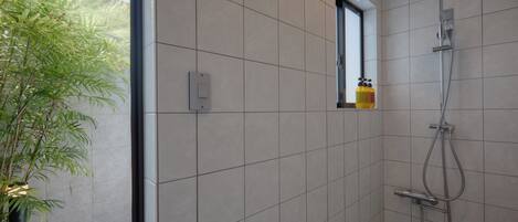 A modern bathroom with a shower, a small window, and a potted plant.