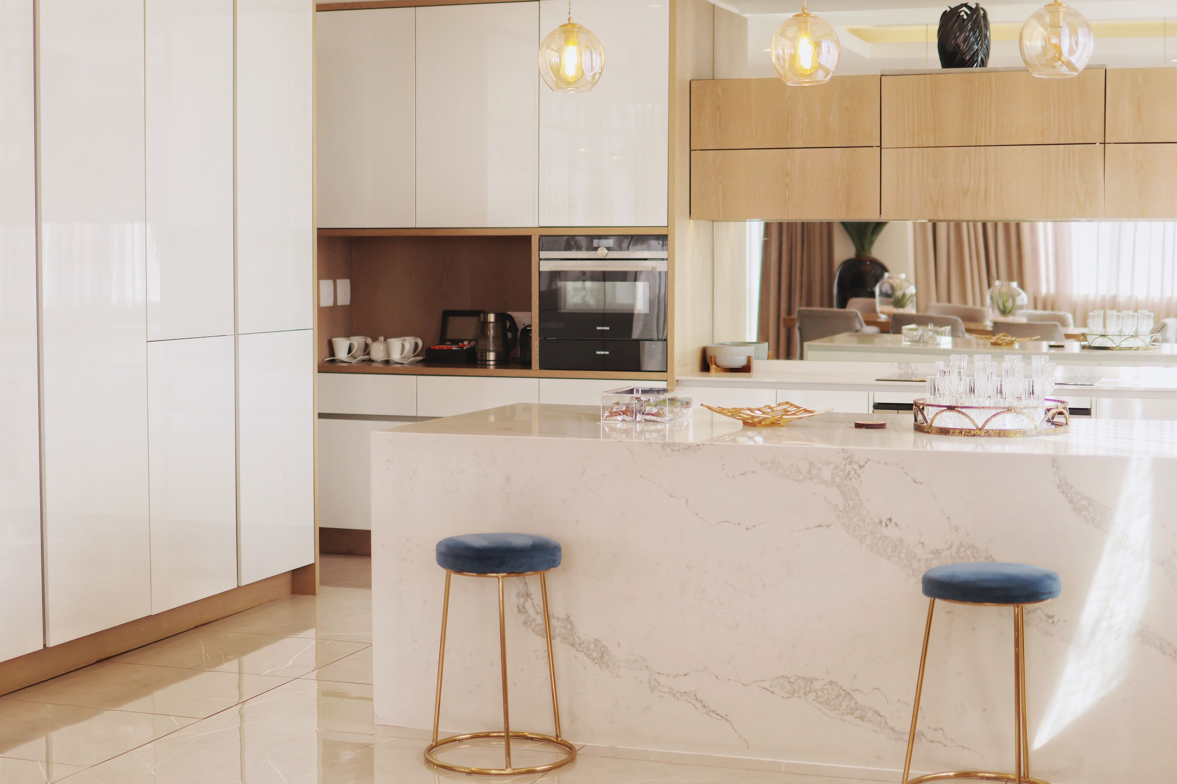 A modern kitchen with white cabinets, a marble island, and two blue bar stools.