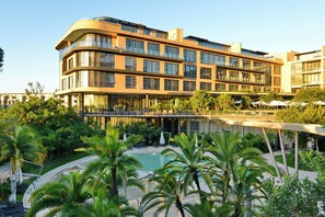 Un hotel modern amb zona de piscina envoltada per palmeres i vegetació.