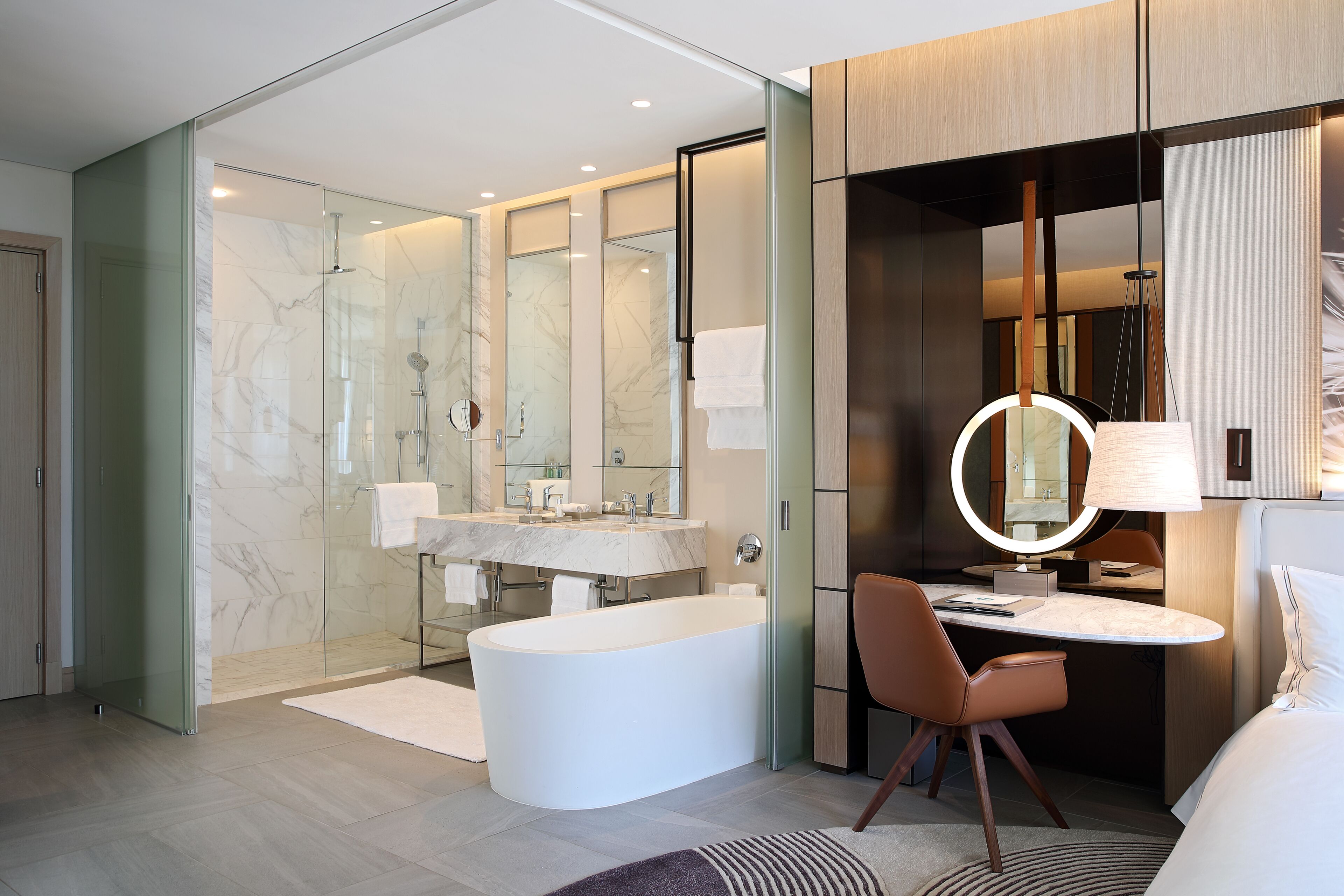Une salle de bain moderne avec une douche à parois de verre, une baignoire sur pieds, un meuble-lavabo avec un miroir et une table ronde avec une chaise.