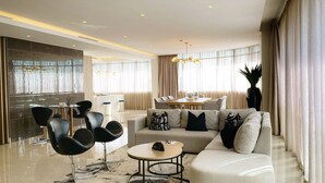 A modern living room with a sectional sofa, black chairs, a round coffee table, and a dining area in the background. - The Houghton Hotel, Spa, Wellness & Golf (Johannesburg)