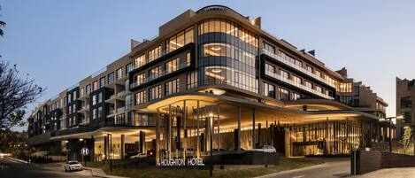 A modern hotel with a curved facade, large windows, and a well-lit entrance.