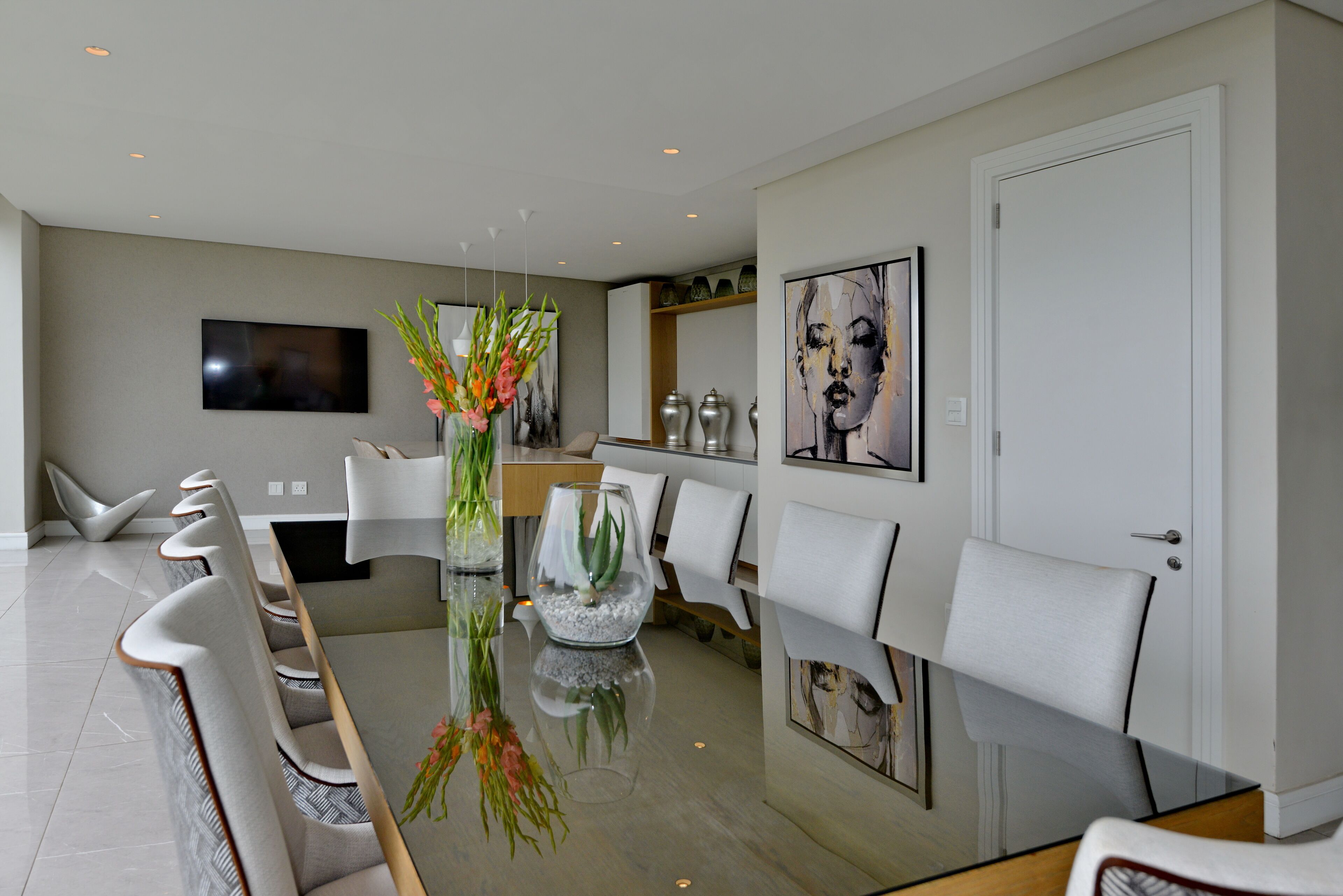 A modern dining area with a glass table, white chairs, and a vase with flowers.