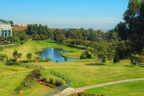 Camp de golf amb un estany, envoltat d'arbres i un edifici al fons.