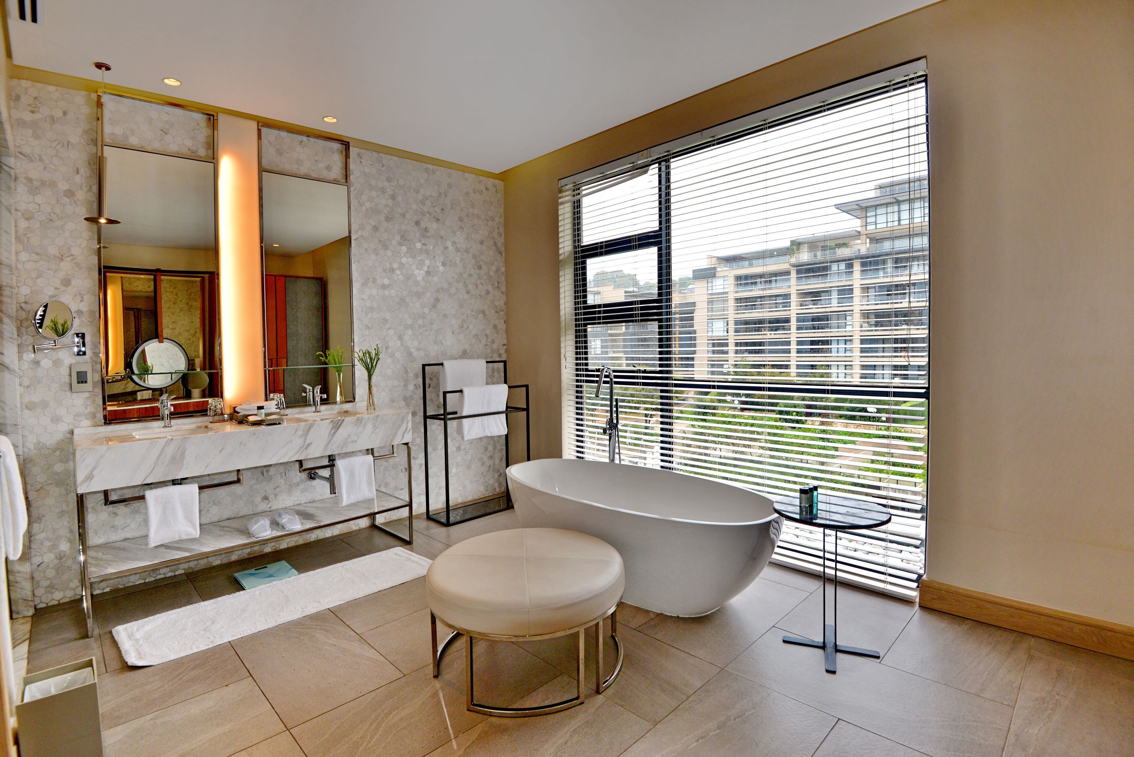 A modern bathroom with a freestanding bathtub, a large mirror, and a window with blinds.