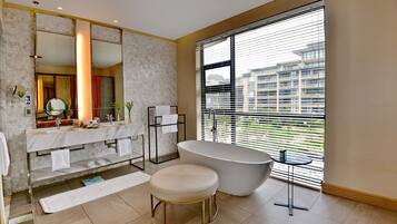 A modern bathroom with a freestanding bathtub, a large mirror, and a window with blinds.