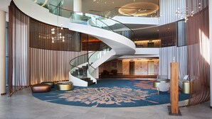 A modern hotel lobby with a curved staircase, a large blue carpet, and contemporary furnishings. - The Houghton Hotel, Spa, Wellness & Golf (Johannesburg)