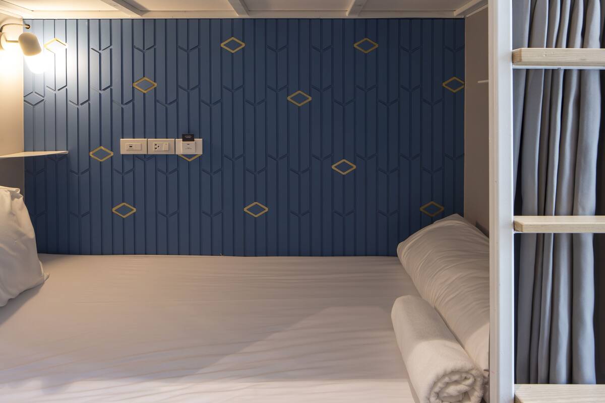 A bunk bed room with a geometric patterned wall, a bedside table with a lamp, and a neatly made bed.
