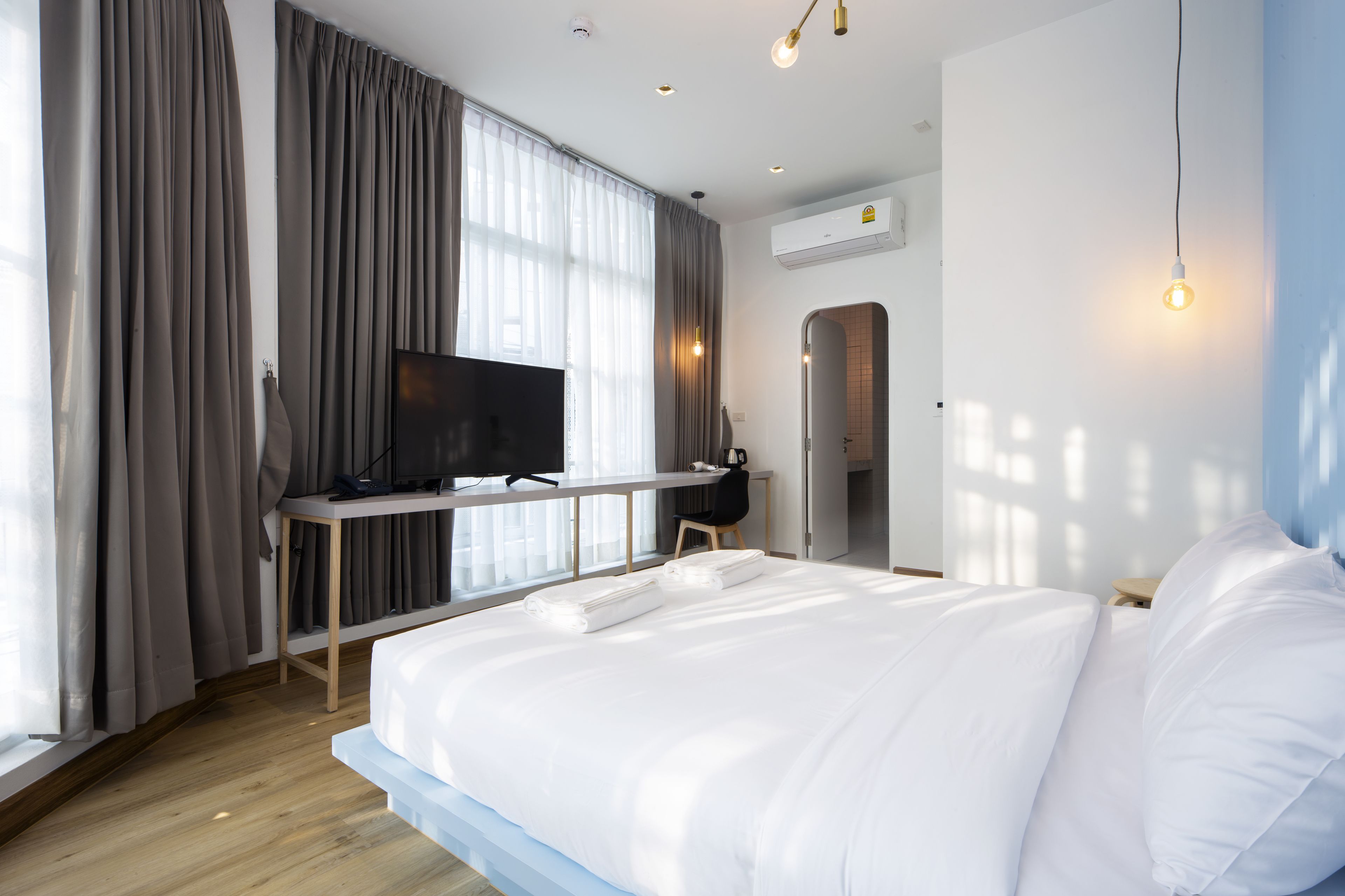 A modern hotel room with a large bed, a desk with a flat-screen TV, a chair, and a window with curtains.