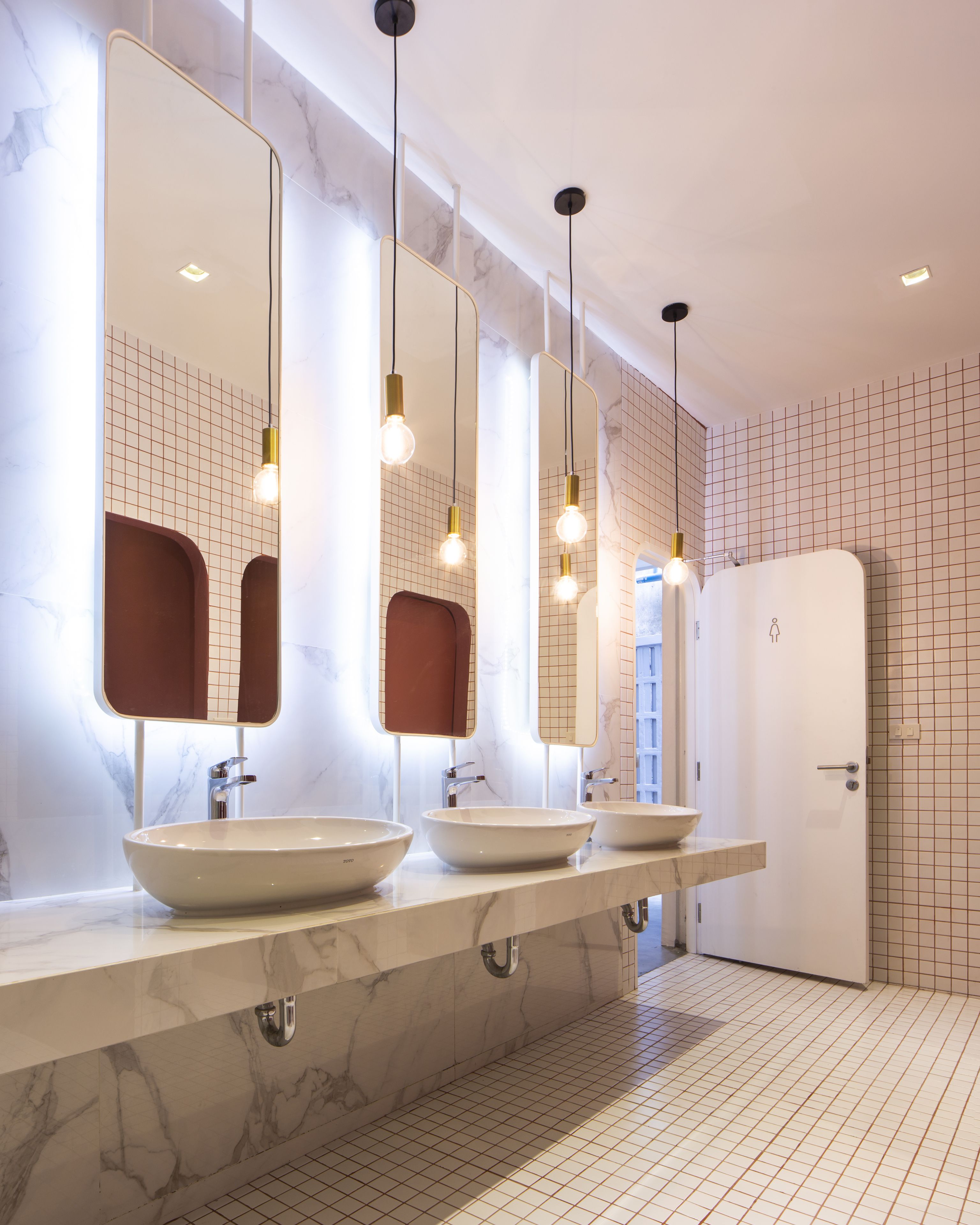 Une salle de bain moderne avec trois vasques, des plans de travail en marbre et des murs à motifs géométriques.