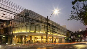 A modern building with a glass facade and multiple levels, featuring a well-lit entrance and visible signage. - Boxpackers Hostel Phranakorn (Bangkok)