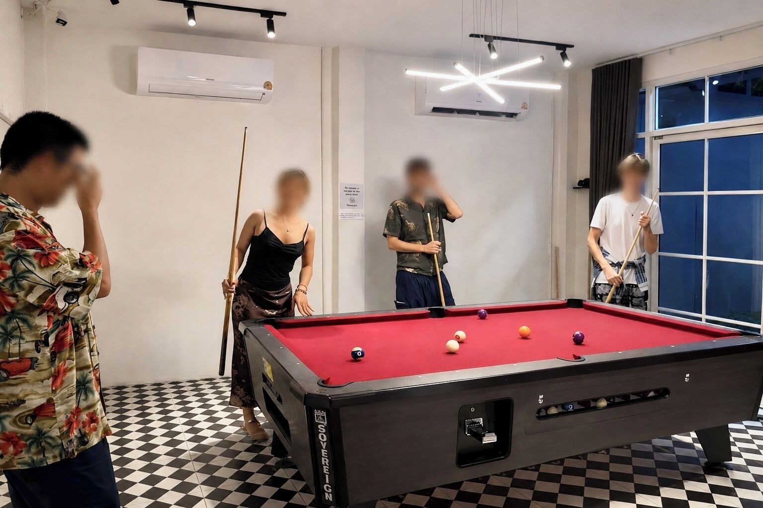 Une table de billard dans une pièce dont le sol est à carreaux, équipée de climatiseurs et dotée d’une fenêtre avec des rideaux.